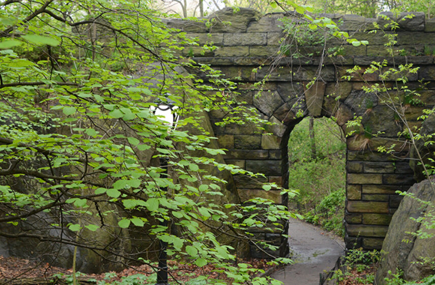 The arch is embedded in a lush green landscape, with a path in the foreground